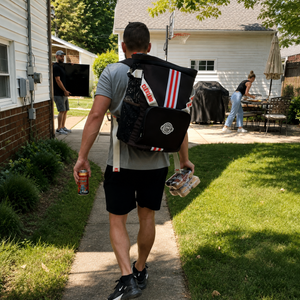 A-man-from-Cleveland-walks-down-a-backyard-pathway-wearing-a-large-Cleveland-backpack-style-messenger-bag-carrier-with-orange-and-white-stripes-and-holding-a-beverage-can-and-a-drink-in-his-hands.Ready-to-tailgate-for-the-Browns.-