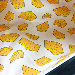 A-close-up-of-a-white-surface-printed-with-Green-Bay-Cheese-Head's-cheese-wedges-in-yellow-and-orange-tones,-with-a-dark-edge-visible-along-the-bottom-right.