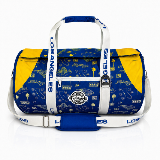 A Los Angeles Rams themed duffel bag featuring a royal blue and yellow football-themed pattern, white handles and shoulder strap with 'LOS ANGELES' text, and a team patch on the front.