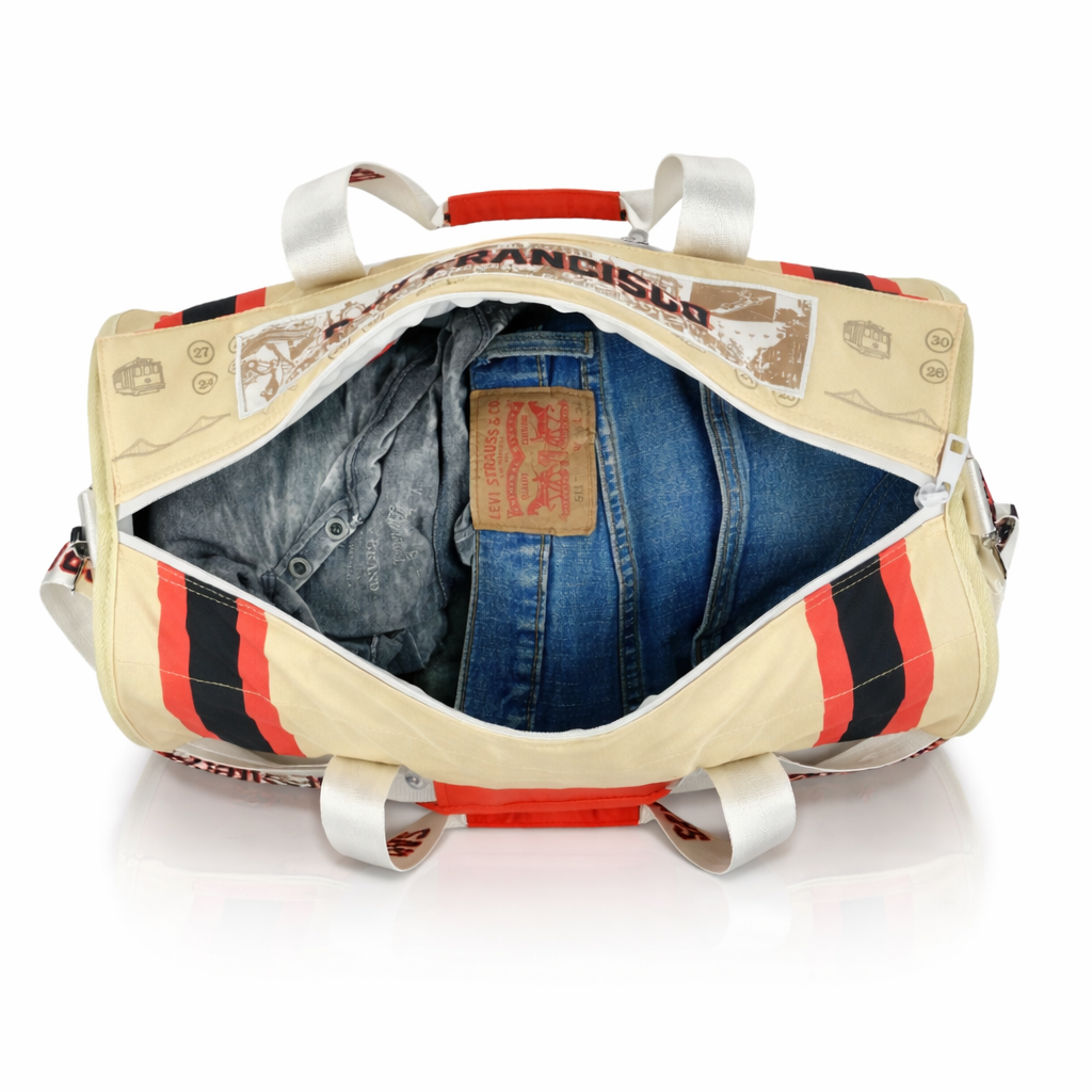 Beige-duffel-bag-with-red-and-black-stripes-containing-blue-jeans-on-a-white-background