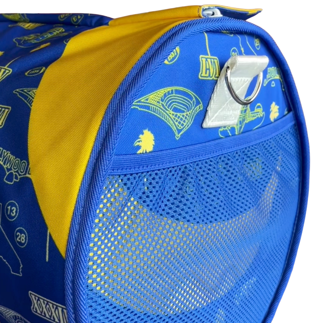 Close-up of a blue and yellow pet carrier bag with a mesh side window, yellow fabric flap, and a white plastic clip with a metal ring on a white background.