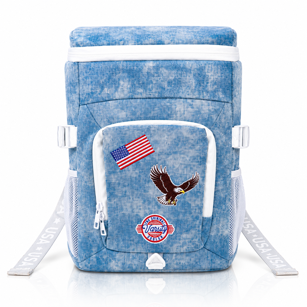 Front view of The Jean Cooler faded blue denim backpack cooler with embroidered American flag, eagle and Varsity Cooler patches.